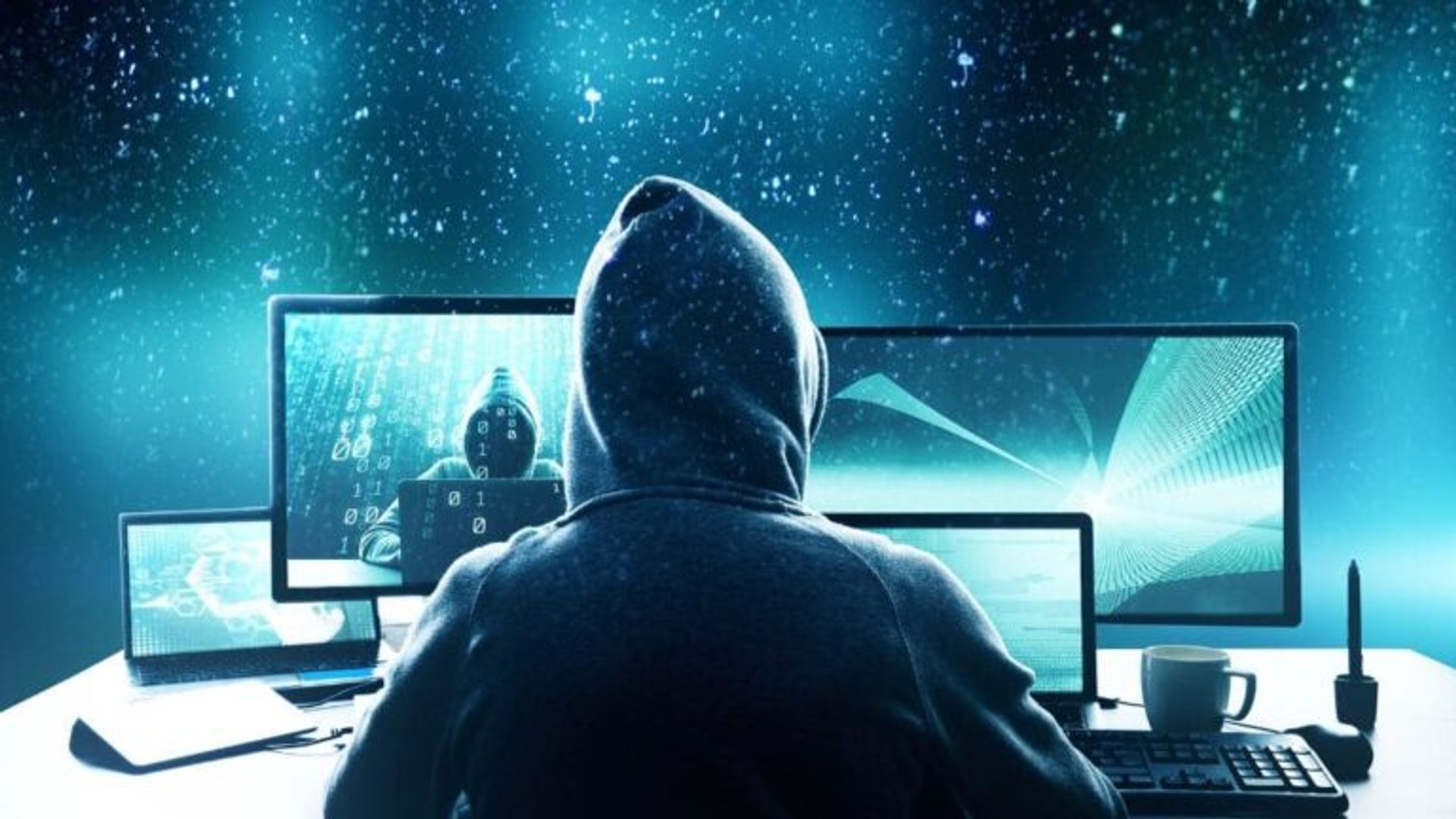 Person in a hoodie working at multiple computer screens displaying code, against a digital background.