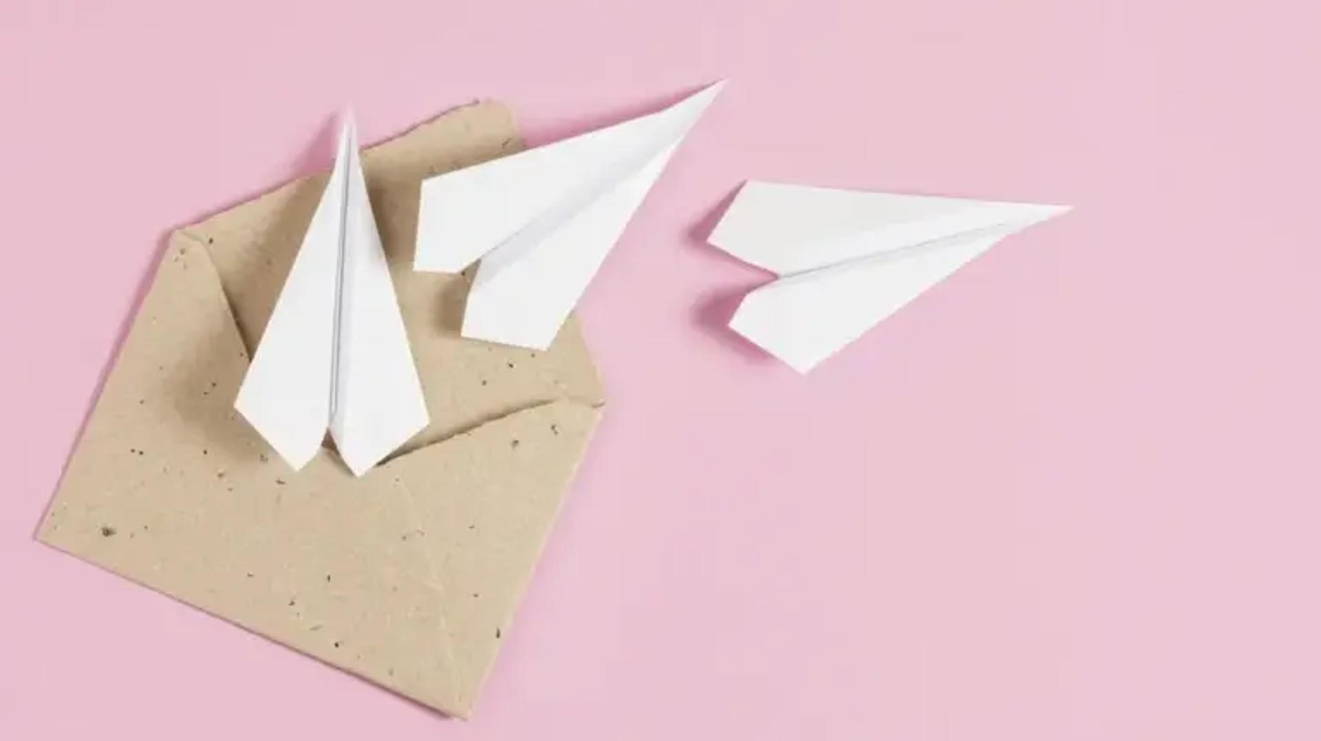 White paper airplanes flying from a brown envelope on a pink background.
