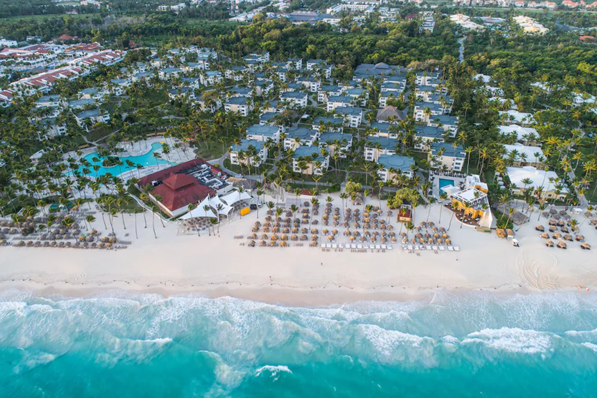 Aerial drone view of the all-inclusive Grand Bavaro Princess resort in Punta Cana, Dominican Republic, featuring lush tropical gardens, numerous low-rise guest buildings, winding swimming pools, expansive white-sand beach, and the turquoise Caribbean Sea.