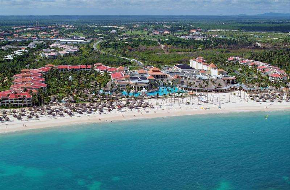 Aerial view of the Paradisus Palma Real Golf & Spa Resort in Punta Cana, Dominican Republic, showcasing its beachfront location, swimming pools, numerous palapas, and surrounding tropical landscape.