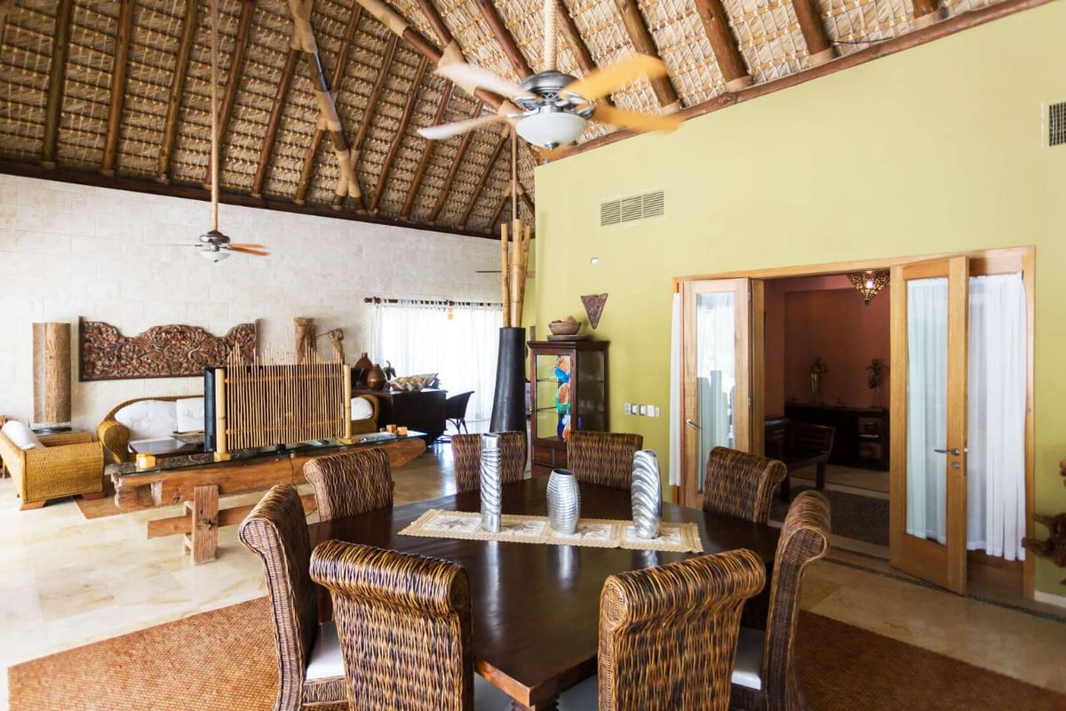 Open-plan dining and living area of the villa beneath a high thatched palm roof