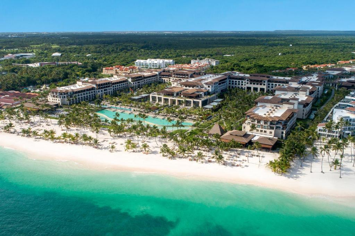 Aerial view of the Lopesan Costa Bávaro Resort, Spa & Casino, showing its beachfront location with white sand, turquoise water, extensive pools, and resort architecture surrounded by lush vegetation.