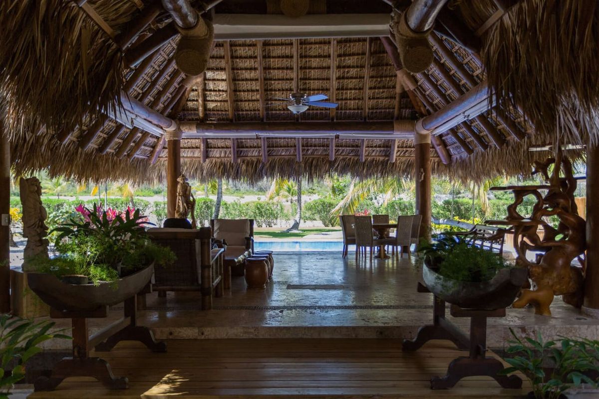 Covered terrace under the thatched roof looking out over the pool and garden