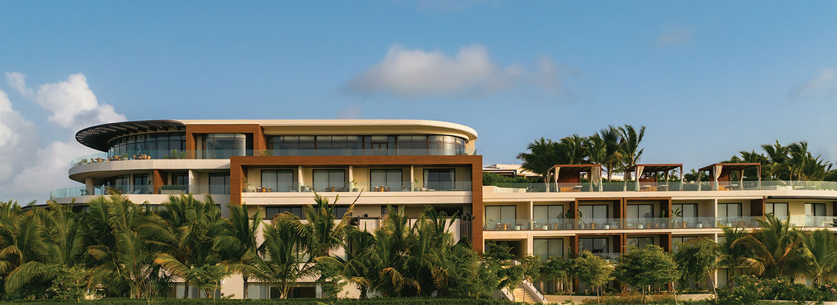 Exterior view of the modern, multi-level facade of The St. Regis resort in Punta Cana, surrounded by lush tropical vegetation with palm trees under a clear blue sky.