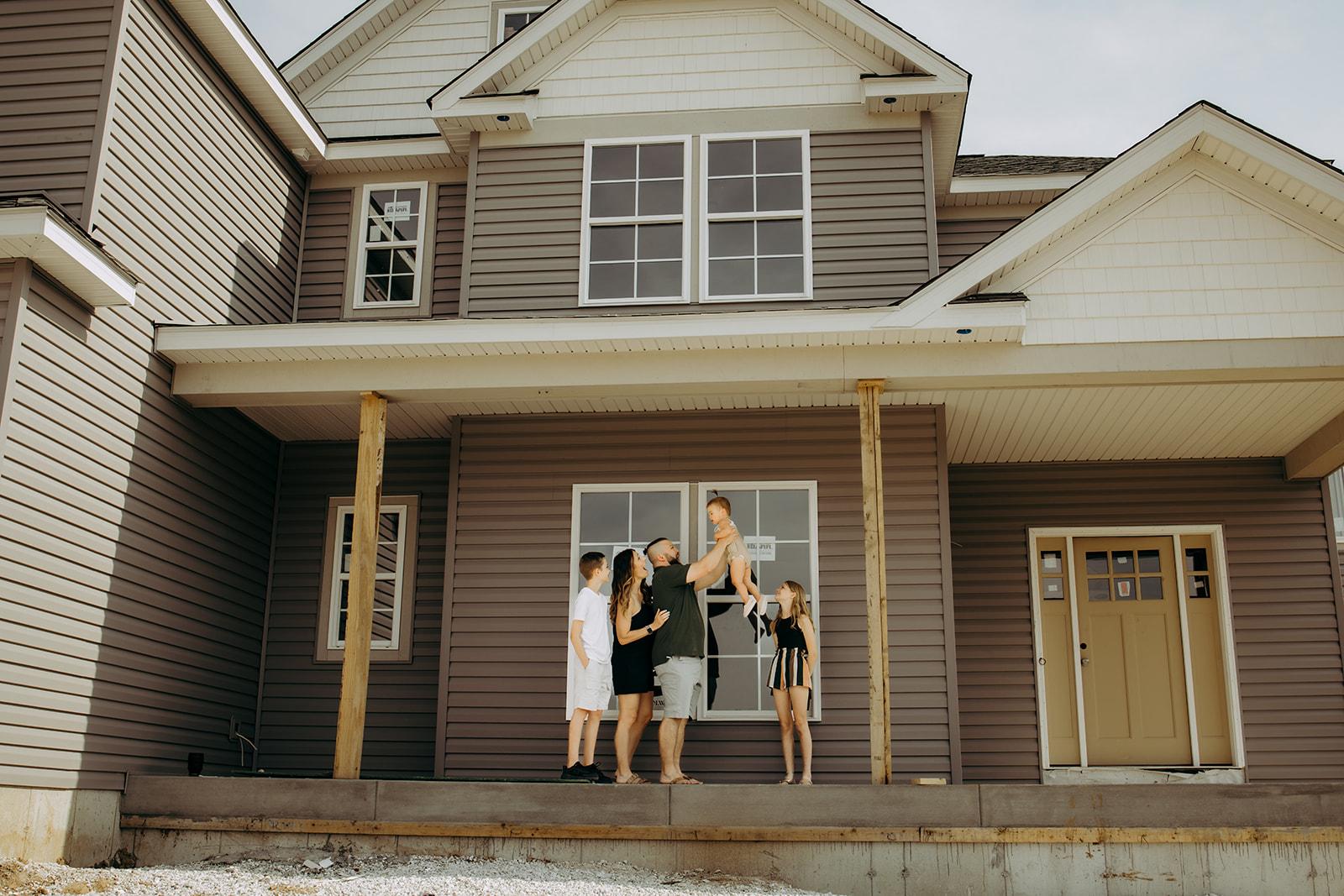 A family celebrates outside their new home featuring a tan exterior.