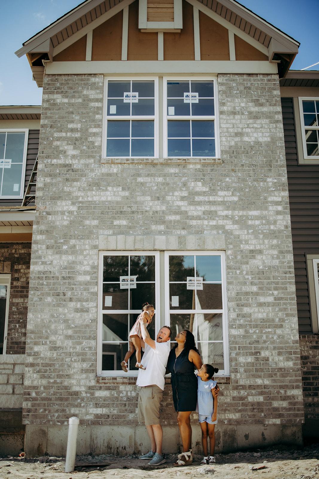A joyful family of four standing in front of their newly constructed two-story Gentry Homes residence in Iowa, featuring brick and siding exteriors, symbolizing new beginnings and homeownership.