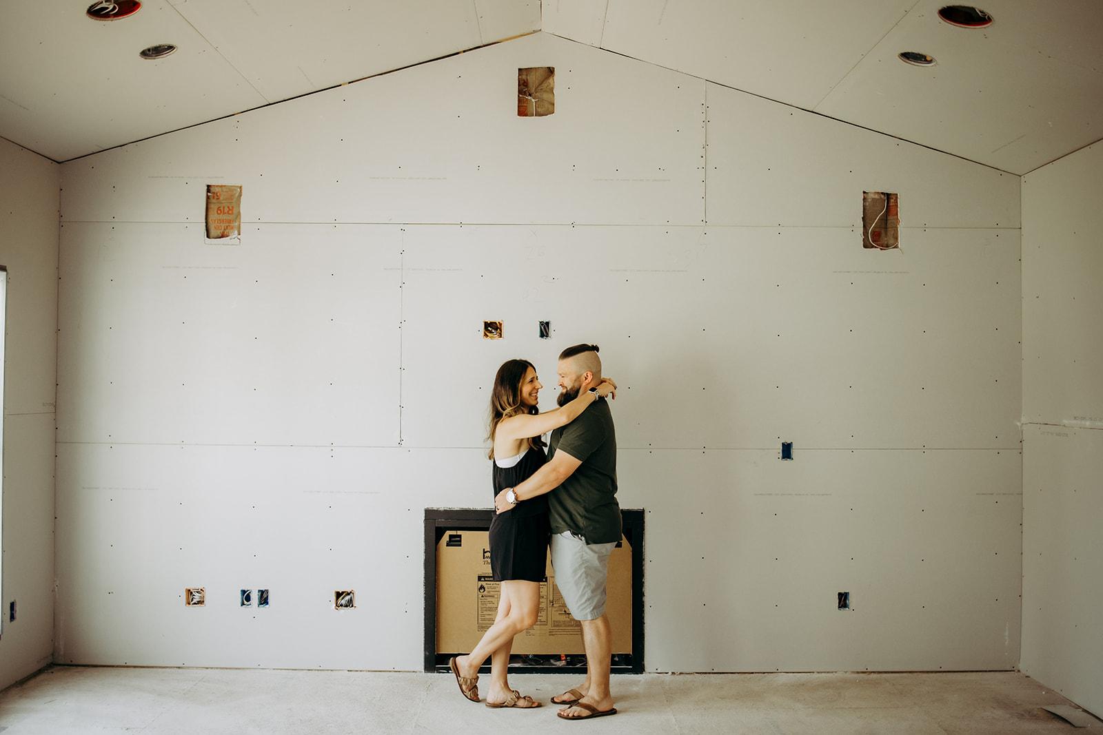 A happy couple embracing in the living room of their newly constructed Gentry Homes residence in Iowa, surrounded by unfinished drywall as they enjoy the excitement of their home’s progress.