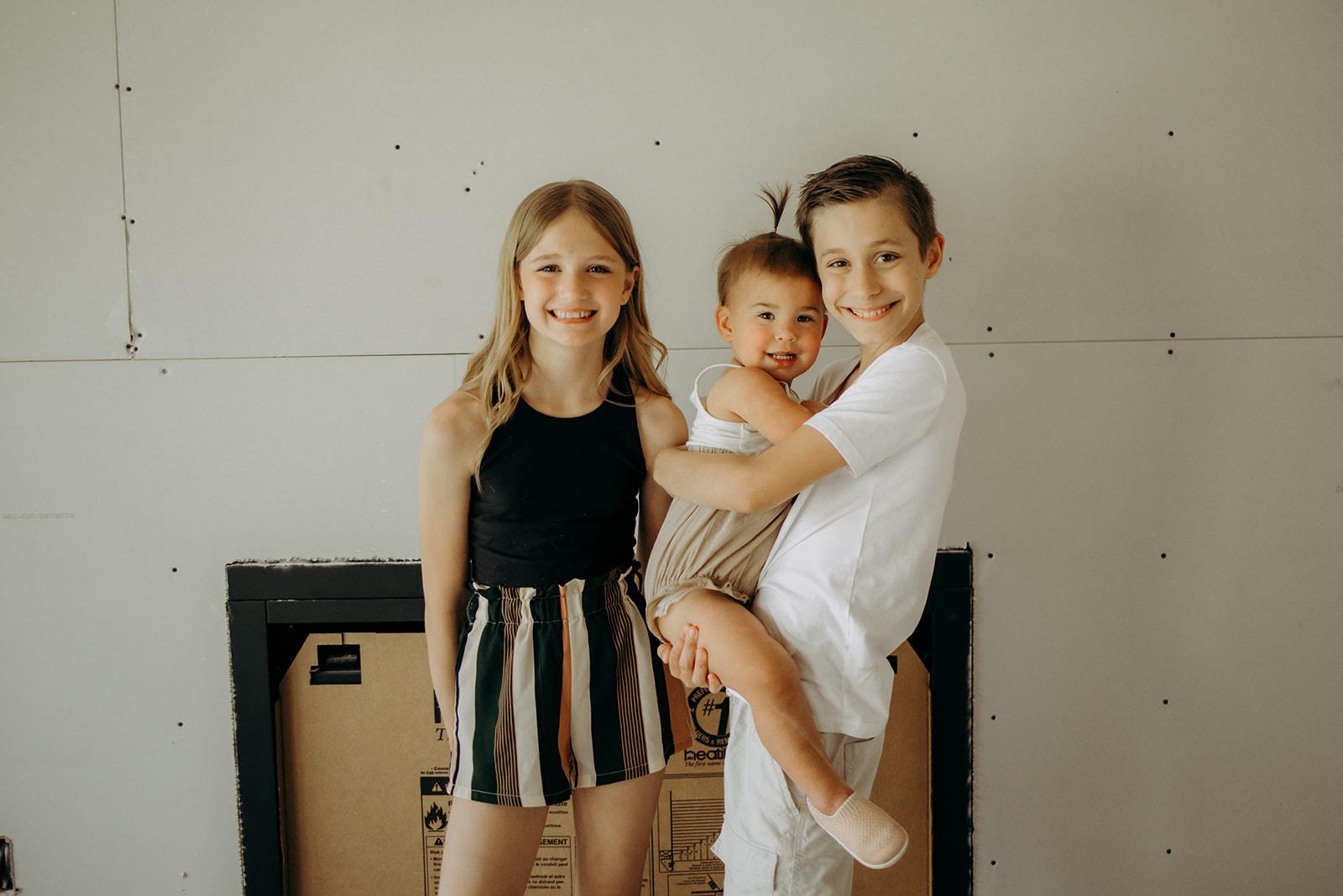 Three smiling children standing together in a newly constructed Gentry Homes residence in Iowa, with unfinished drywall in the background, representing family-friendly home building.