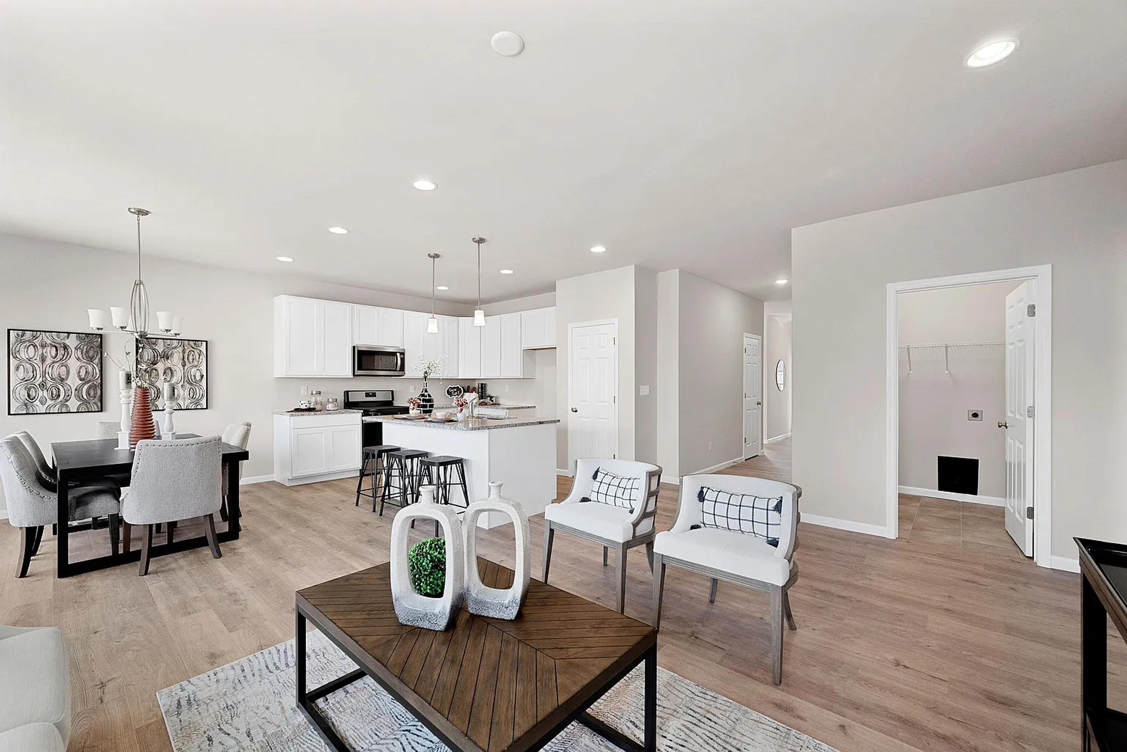 Modern open-concept living space with a cozy seating area, a dining table, and a bright kitchen featuring white cabinets, stainless steel appliances, and pendant lighting, all complemented by natural light.