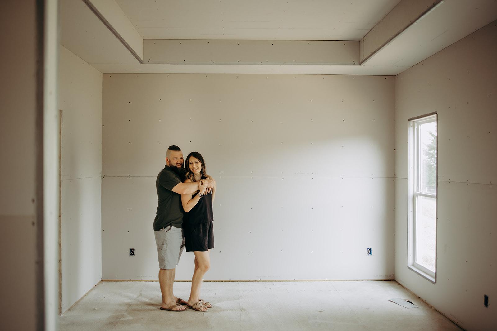 A happy couple embracing in the living room of their newly constructed Gentry Homes residence in Iowa, surrounded by unfinished drywall as they enjoy the excitement of their home’s progress.