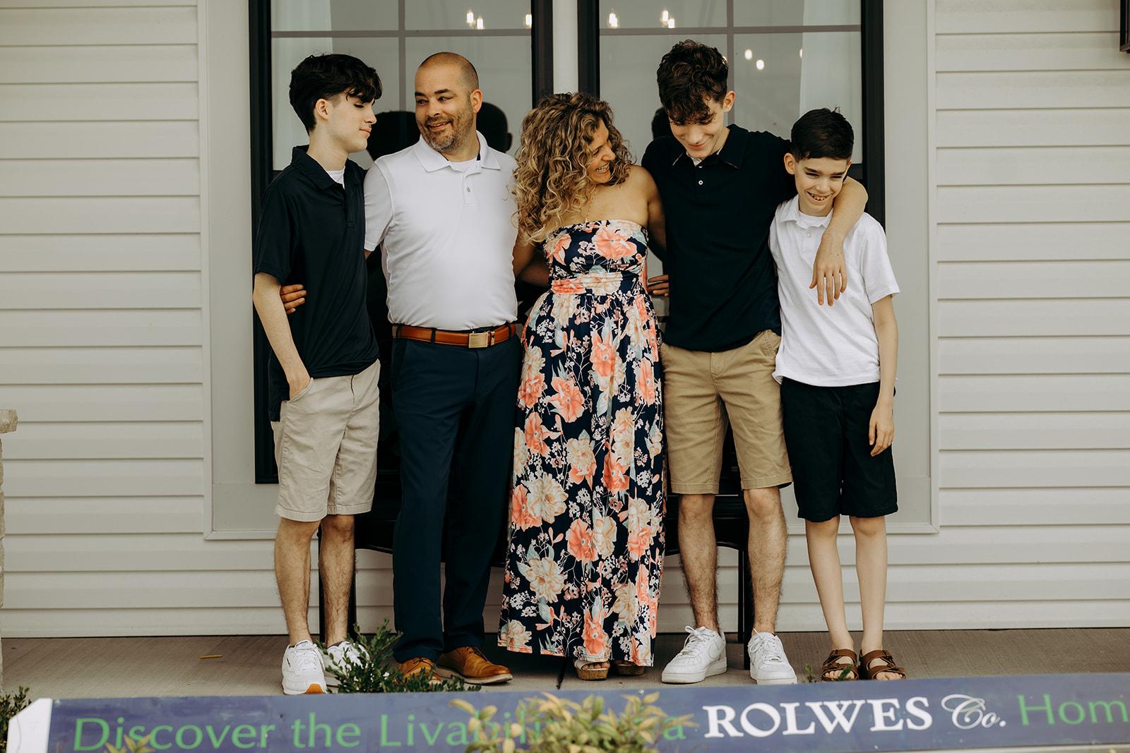 A happy family of five standing together in front of their new Gentry Homes residence, embracing and smiling, symbolizing the joy of homeownership in Iowa