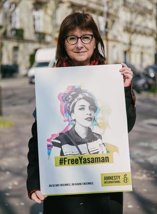 A photo of a women holding a sign that has a graphic drawing of Yasaman with the words #FreeYasaman