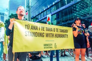 two people hold a banner which reads "standing with humanity" in English and te reo Māori