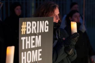 A sign reading "bring them home" and a woman holding a candle