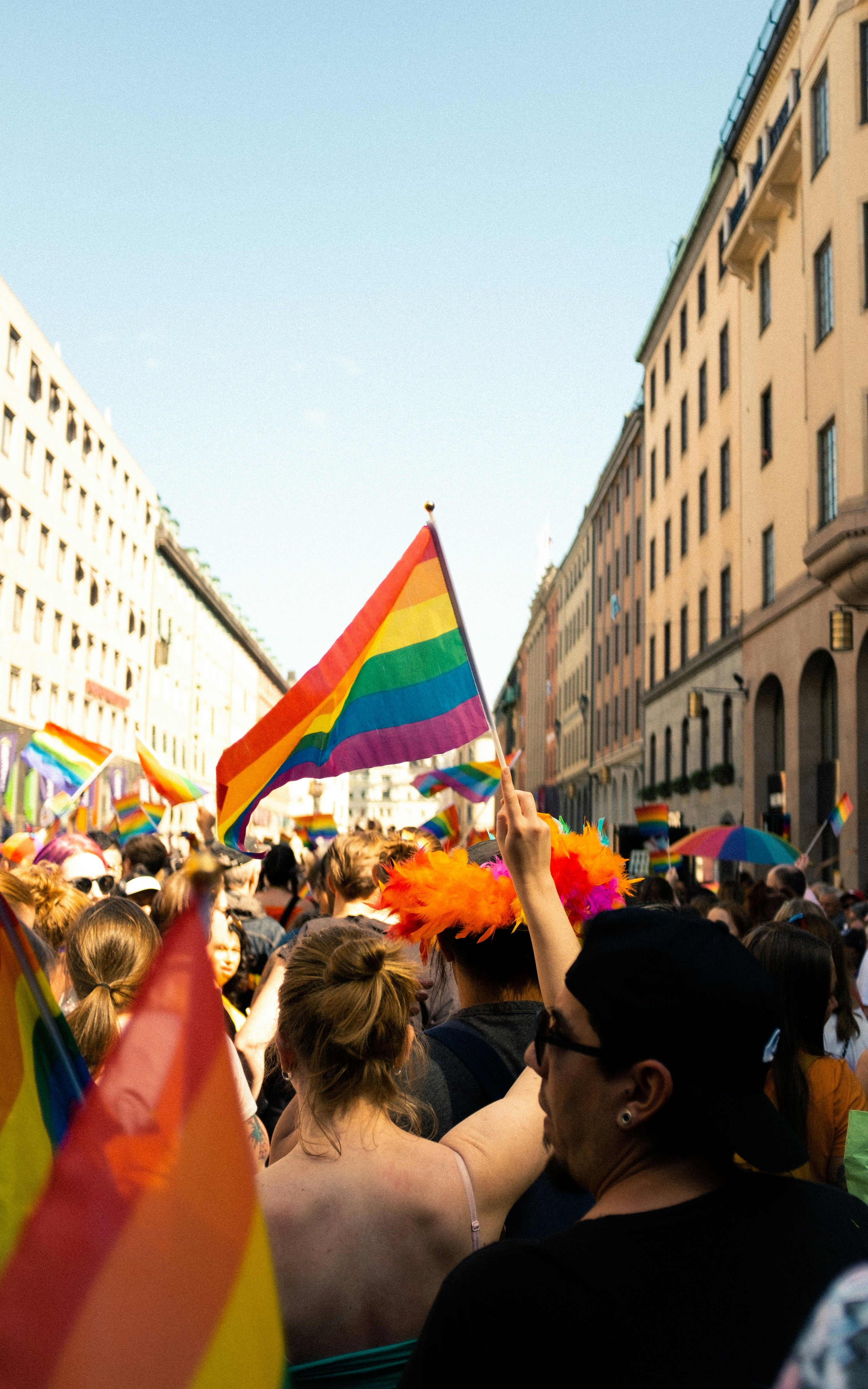 Crowd at a Pride parade, someone holds a rainbow flag.