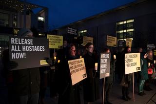 A group of people stand in the dark holding signs calling for an end to the conflict