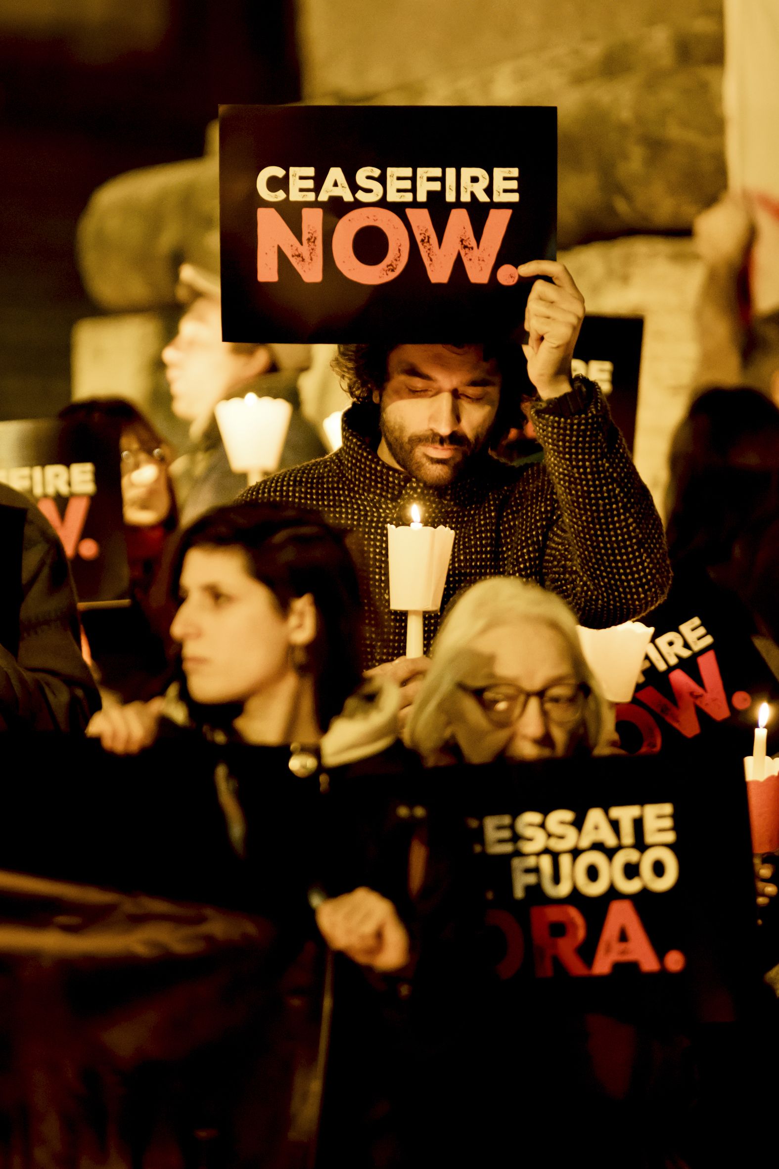 A person holds a sign that reads "ceasefire now"