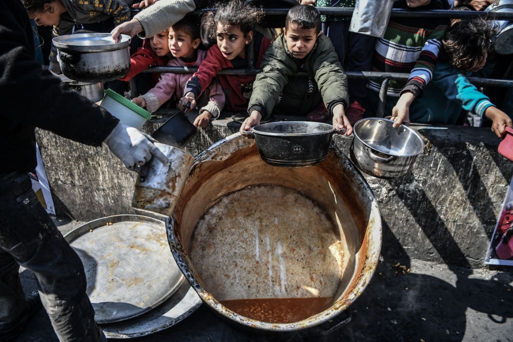 Palestinians hold out their empty containers to be filled with food, distributed by charity organizations