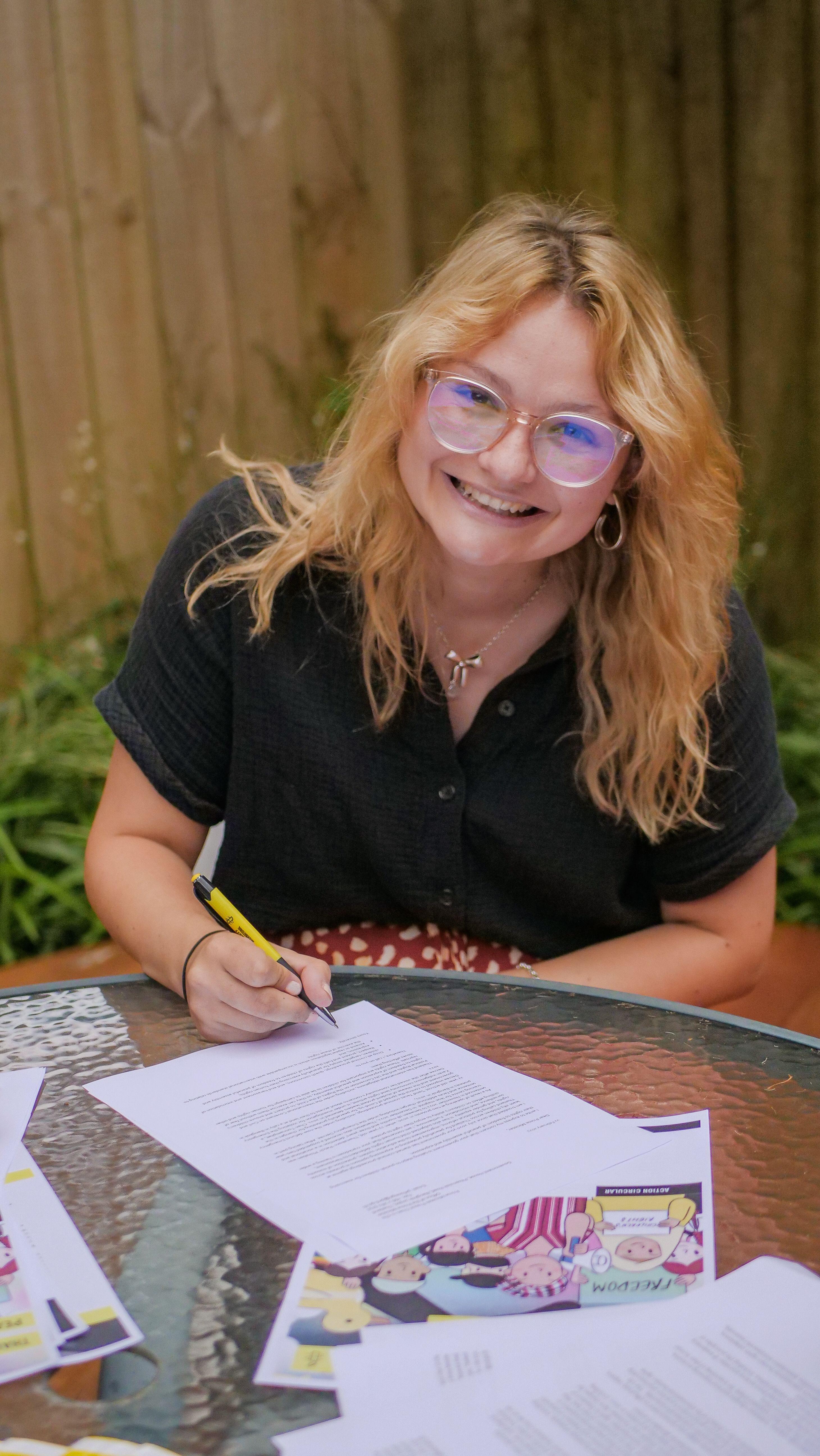 a person with long blonde hair smiles while signing a petition