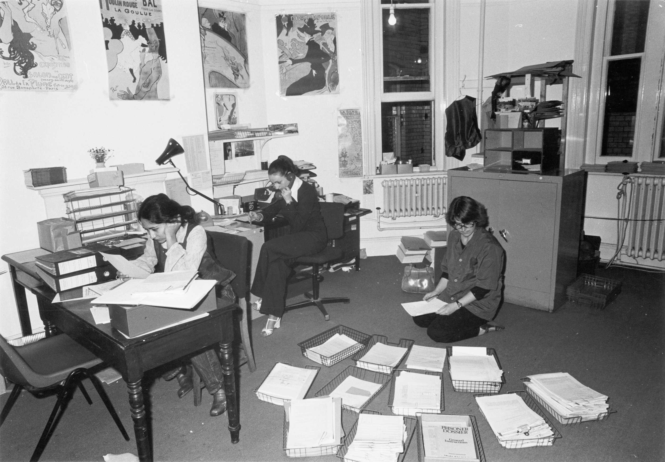 three people work in an Amnesty office sorting paper and answering phone calls