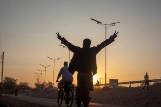 The silhouette of a person with a sunset in the background, they have their back turned to the camera with two arms in the air doing the peace symbol