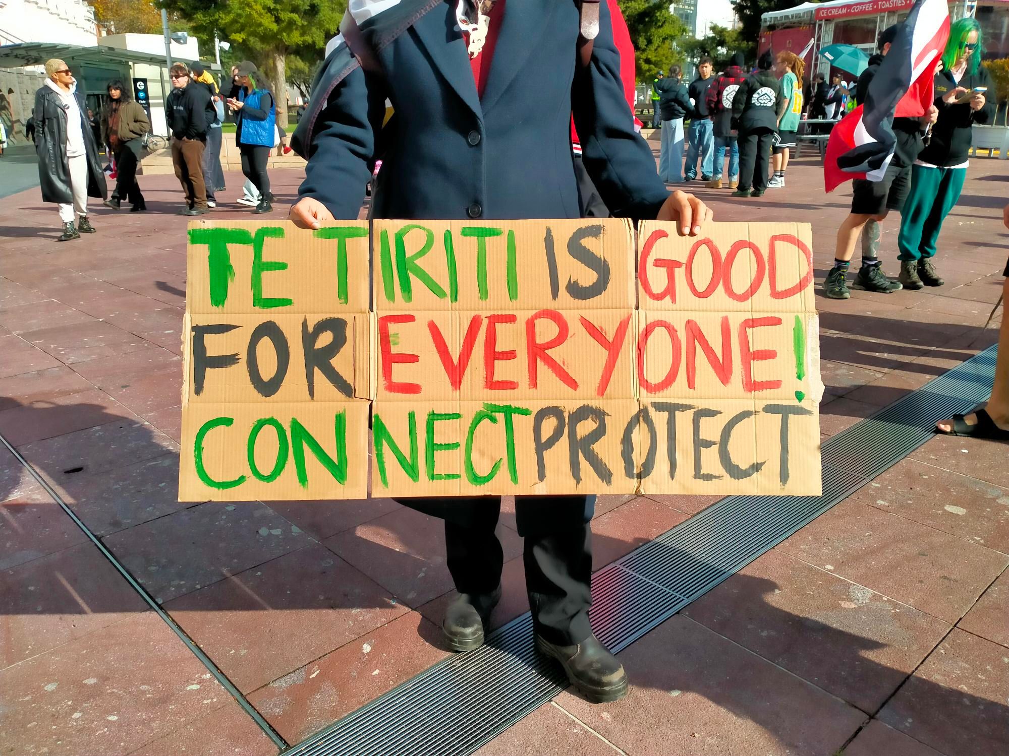 A person holds a sign that reads "Te Tiriti is good for everyone, connect, protect"