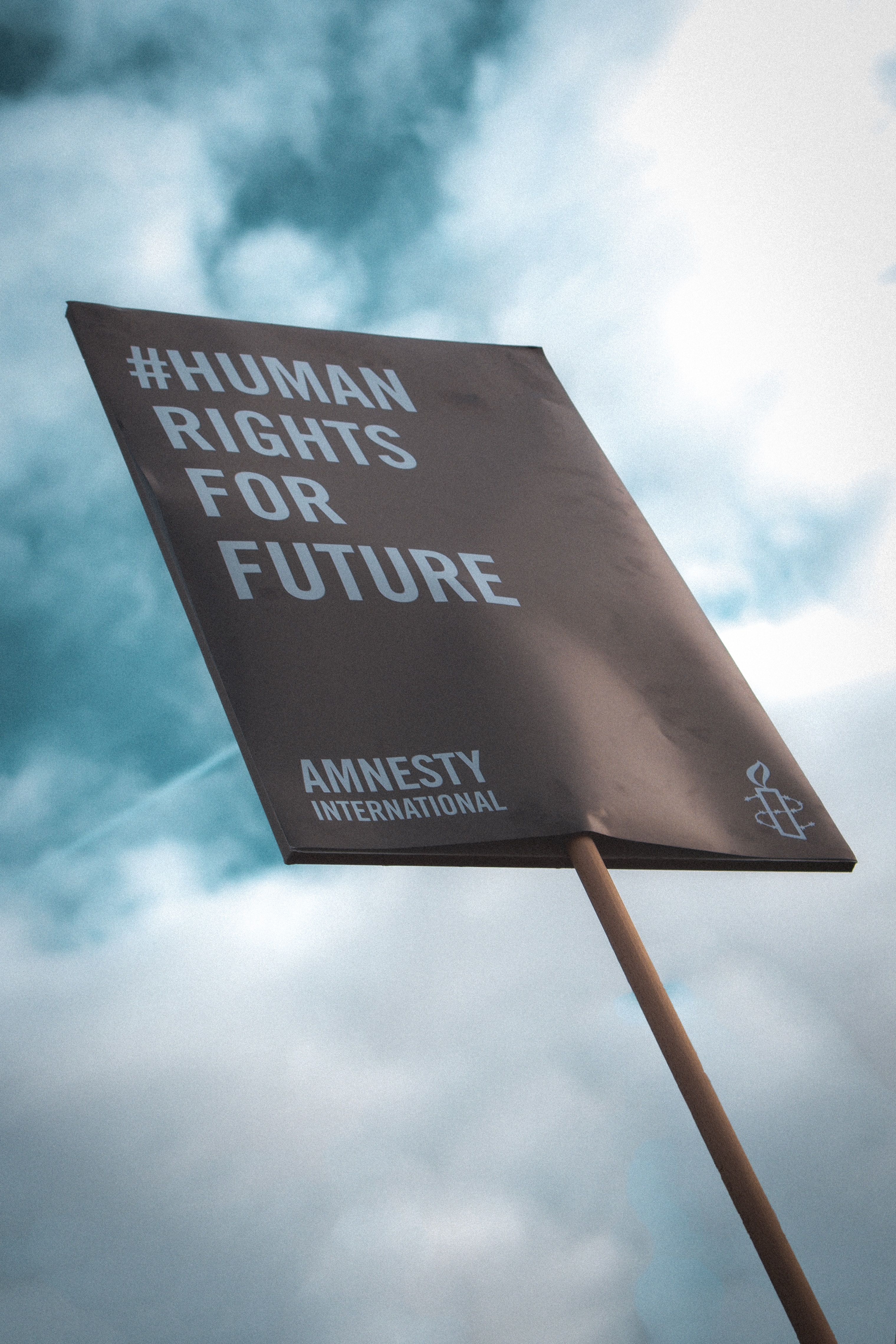 A sign reads Human Rights for Future and is held against a blue sky with white clouds