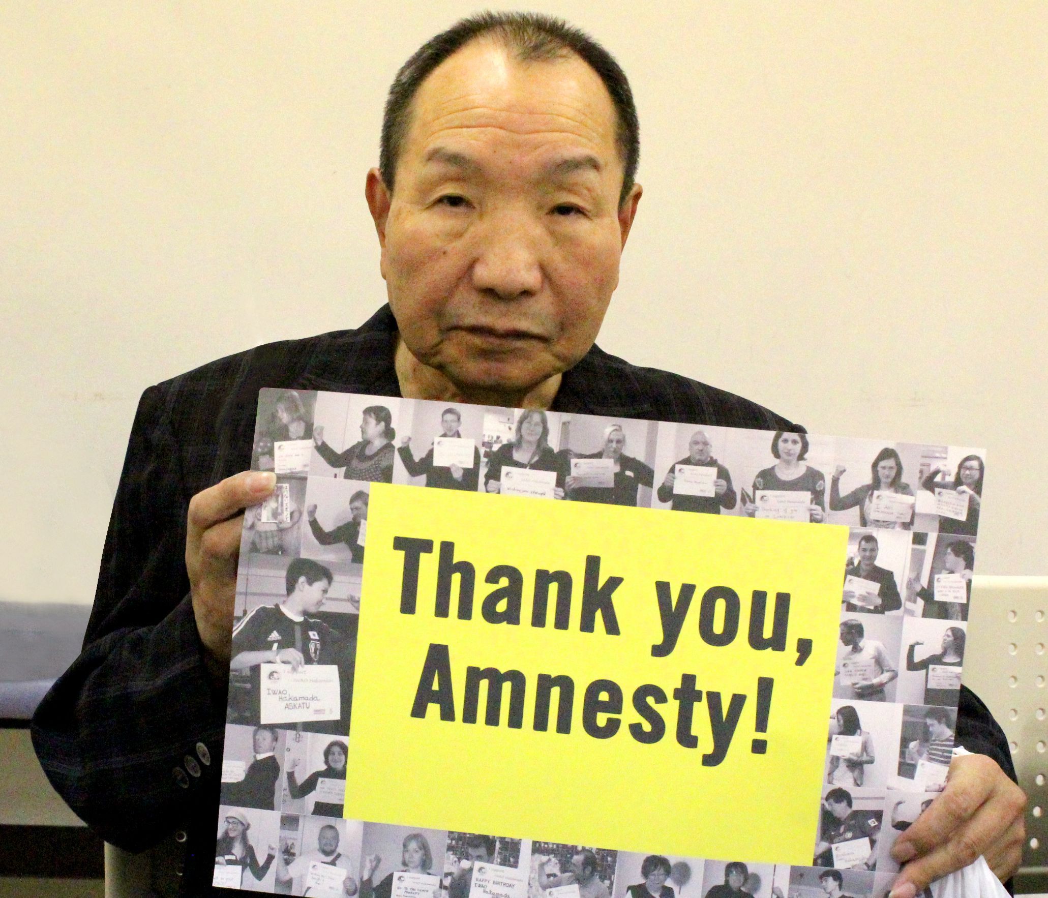 hakamada iwao looking at the camera holding a sign that says 'Thank you Amnesty!', the words are surrounded by photos of people taking action for him over the years. 