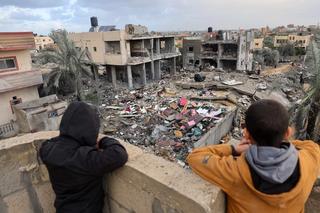 Palestinian children look on as people stand on the rubble of a building destroyed during Israeli strikes on Rafah, on the southern Gaza Strip