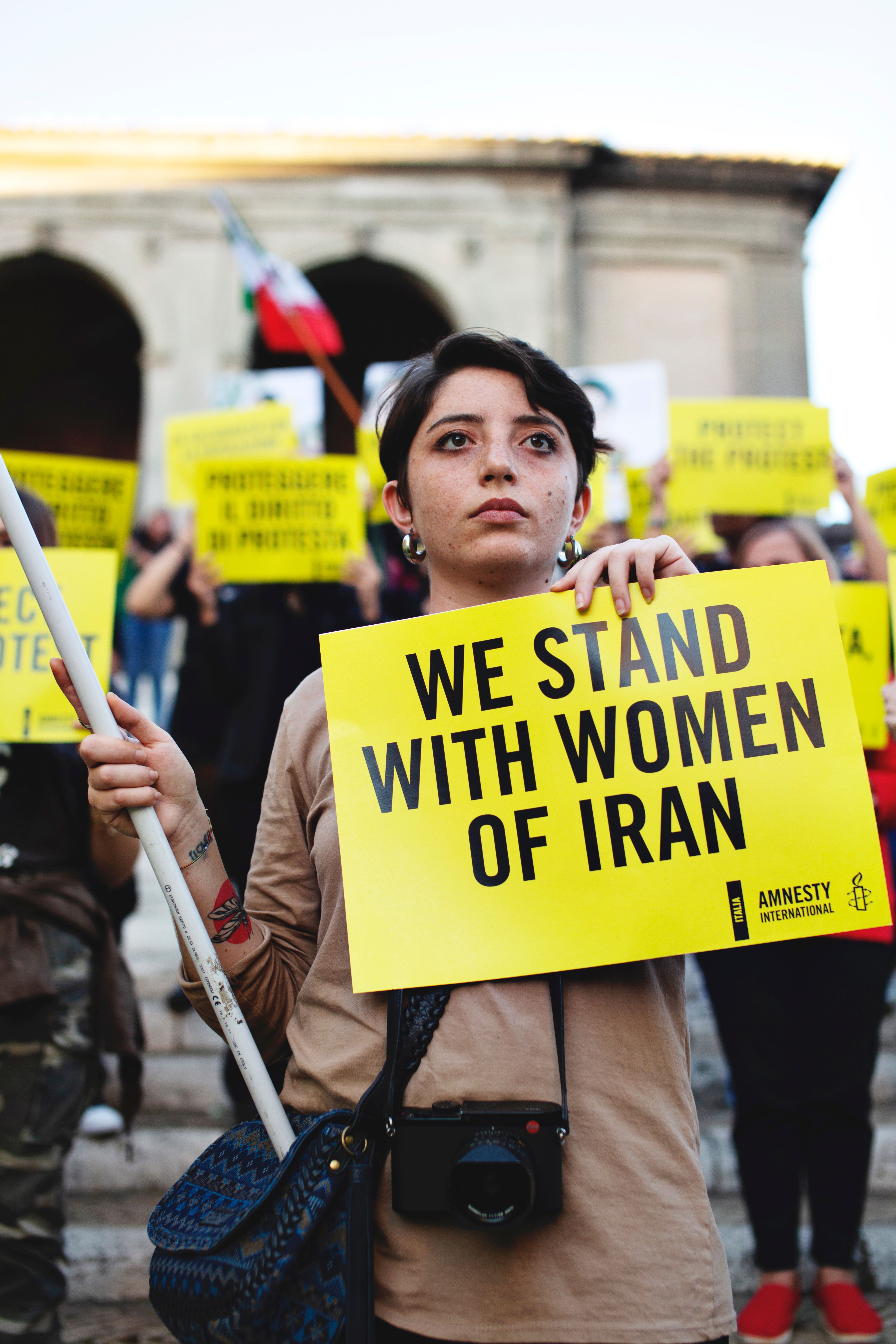 a woman holds a sign that says "we stand with women of iran"