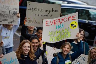 a group of people hold signs calling for human rights and justice while smiling at the camera