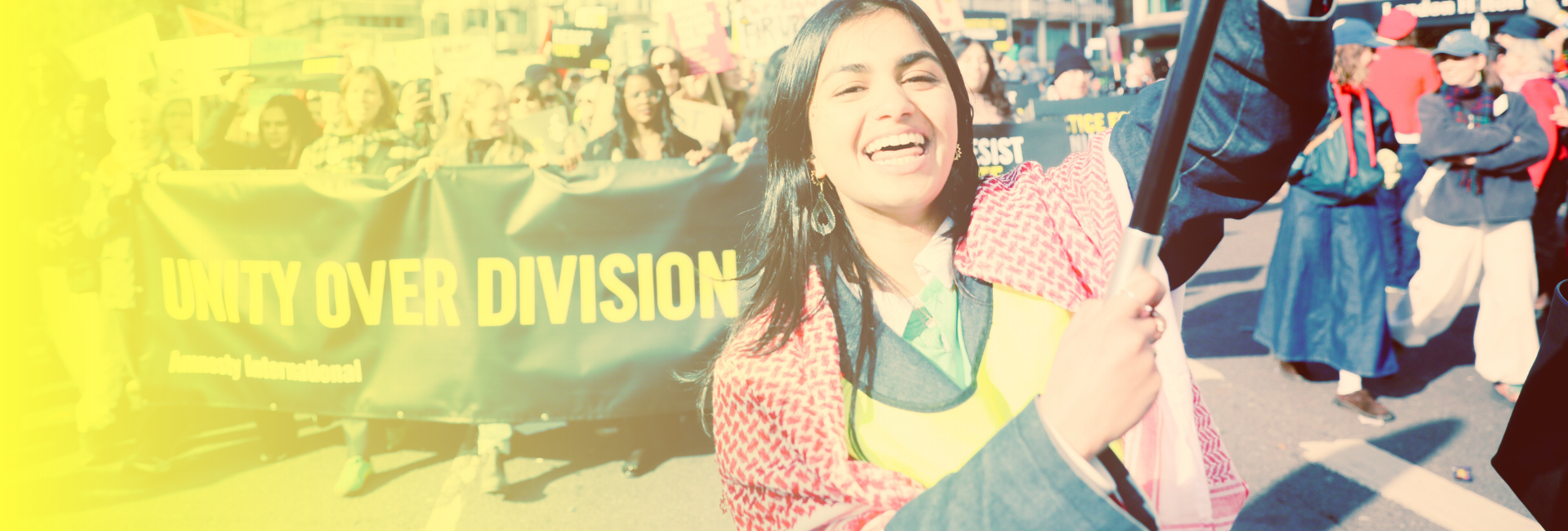 smiling female activist holding a banner and large banner in background that reads unity over division
