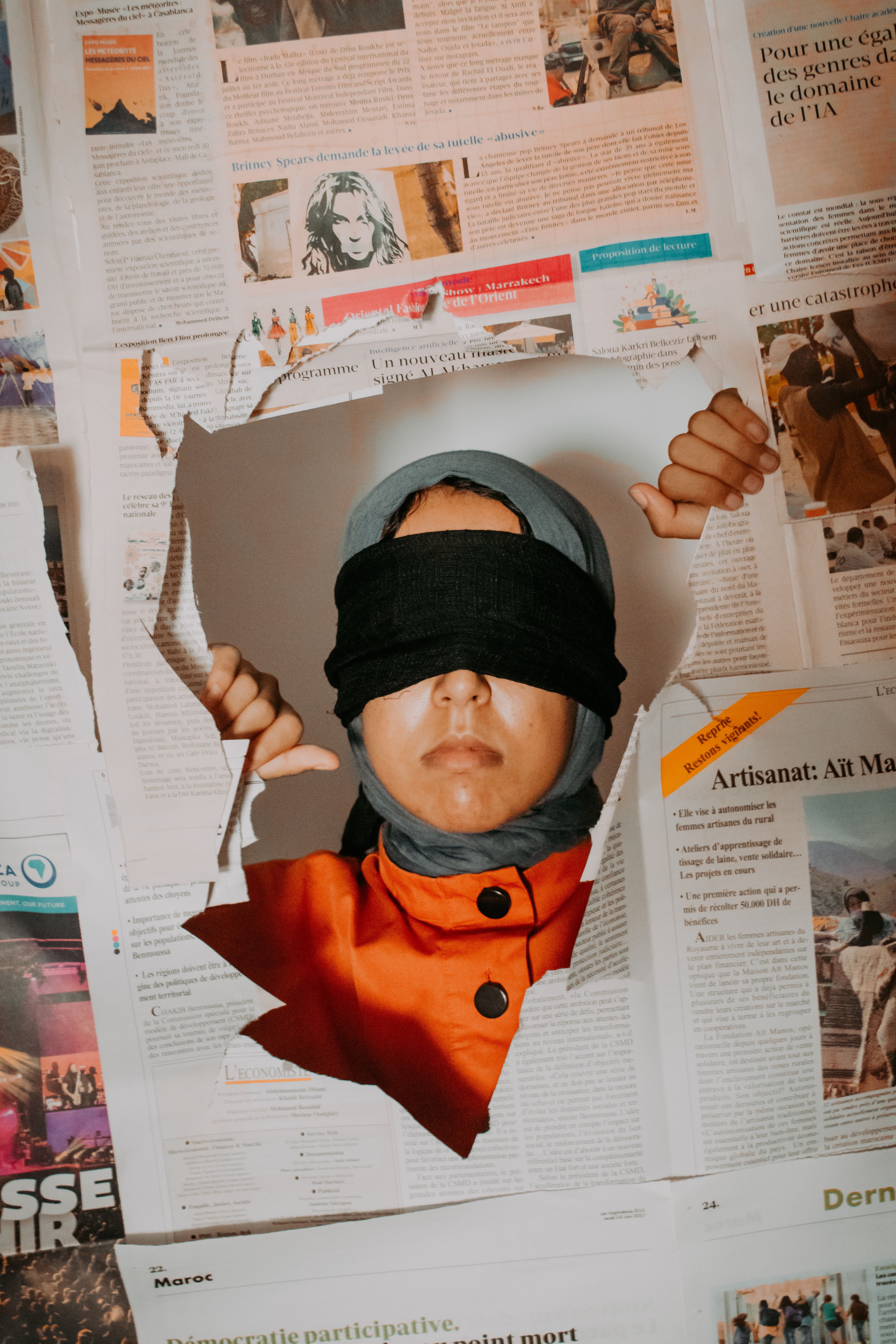 Blindfolded woman looks through newspaper