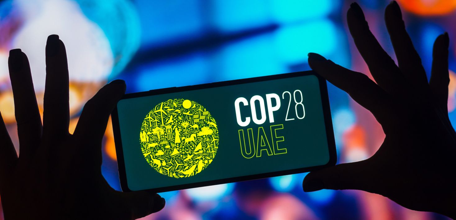 Photo of hands holding up a phone that displays a graphic saying COP28 UAE.