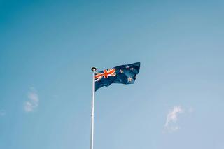 A New Zealand flag flies against a blue sky