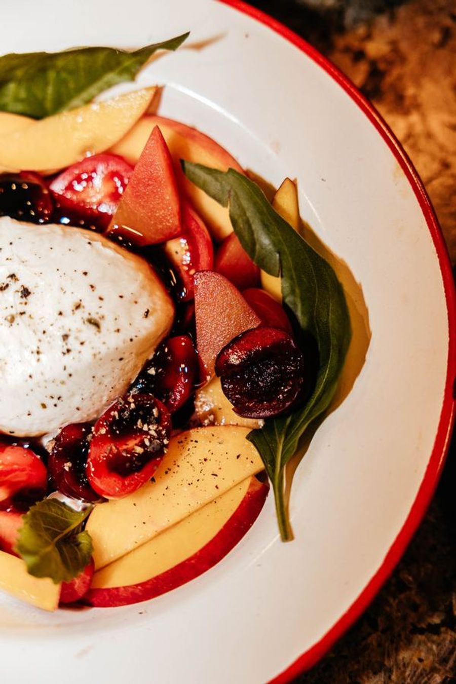 Burrata plated with stone fruit, berries, and basil