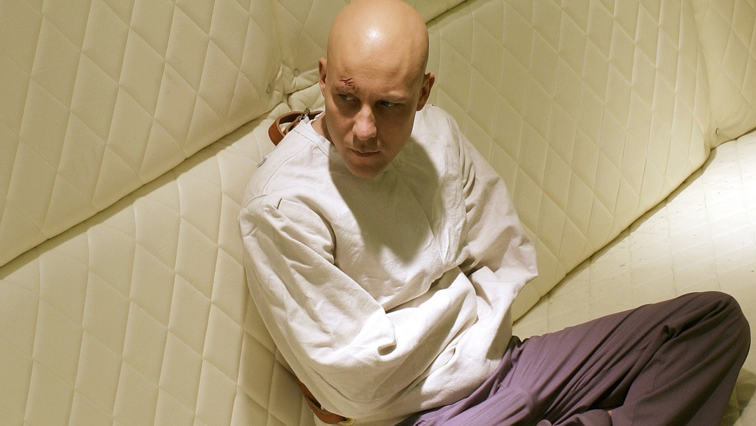 A bald man sitting in a padded cell.