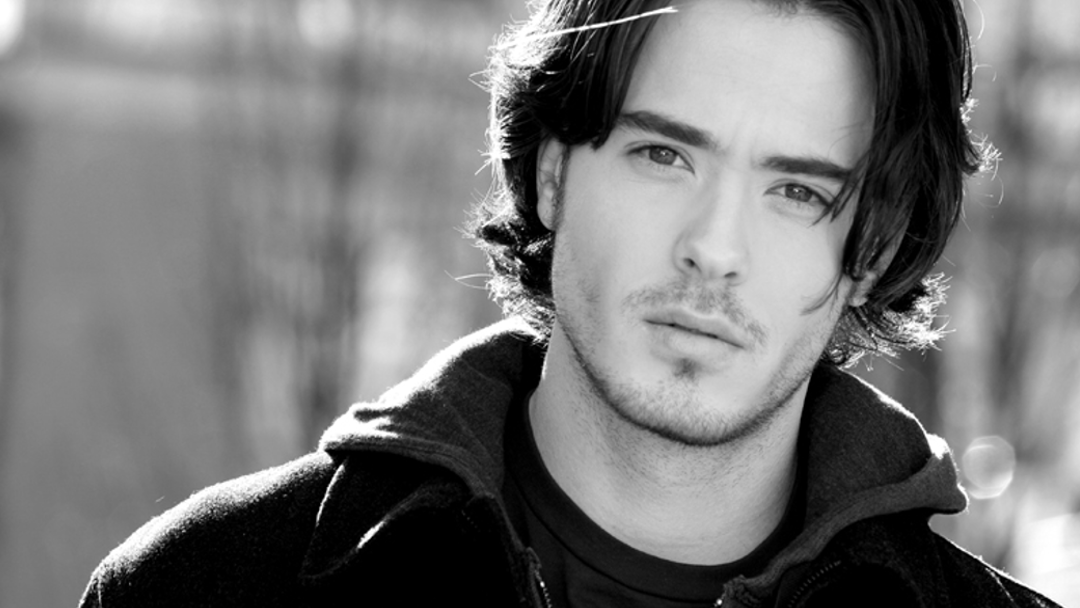 A black and white photo of a young man with hair below his ears.