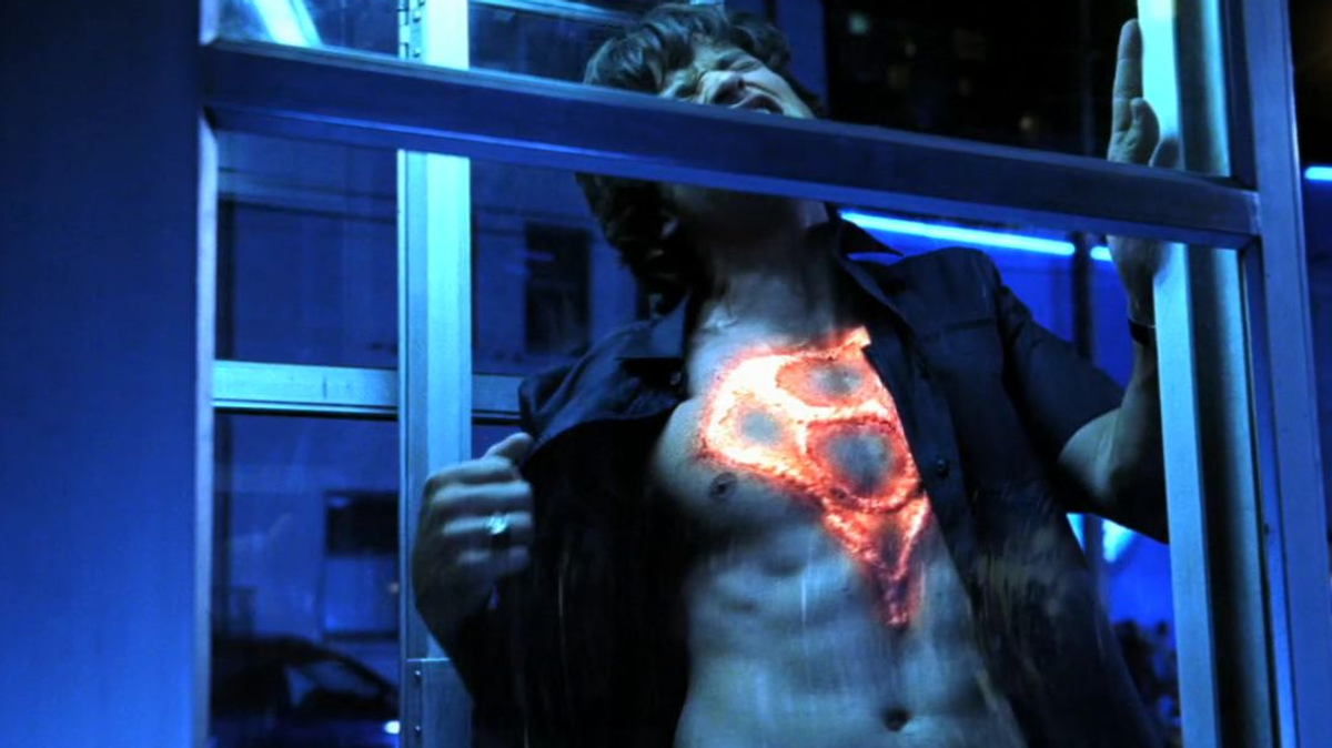 clark kent in a phone booth opening his shirt to reveal the mark of el branded on his chest