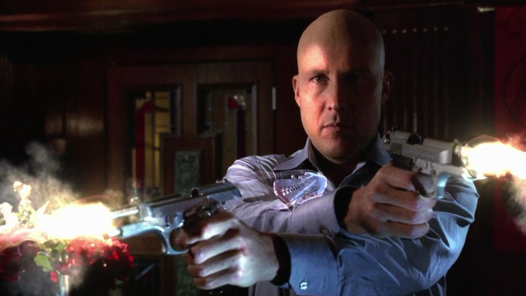 A bald man is firing off dual handguns.