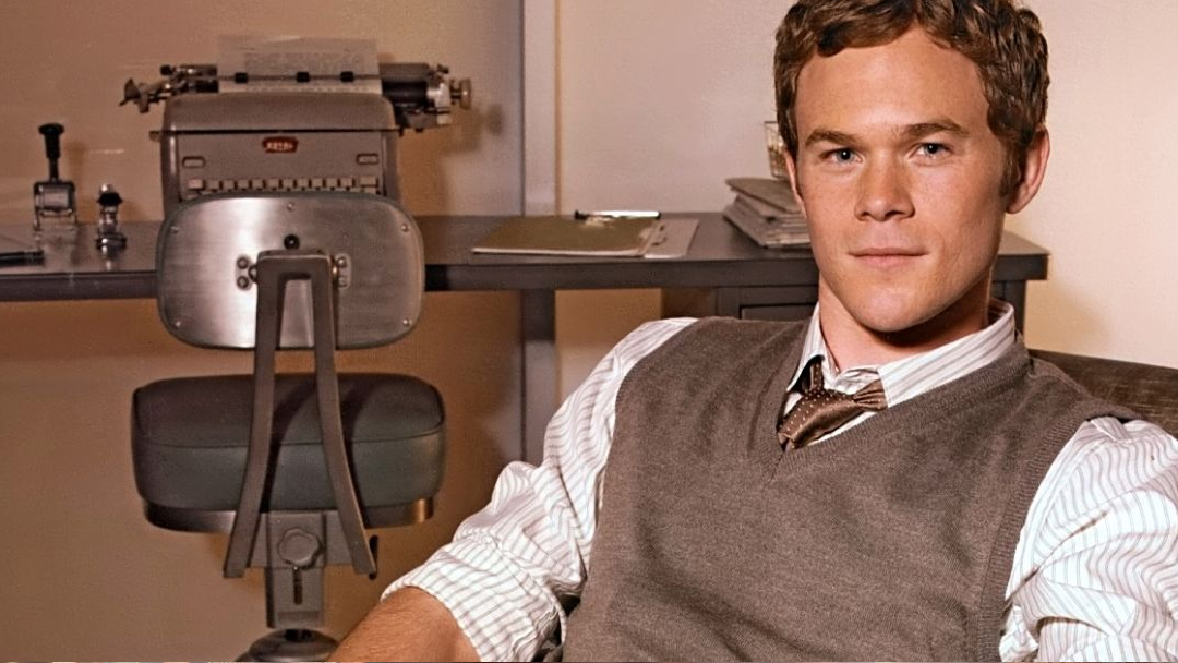 A man in a sweatervest is sitting in front of an old fashioned typewriter.
