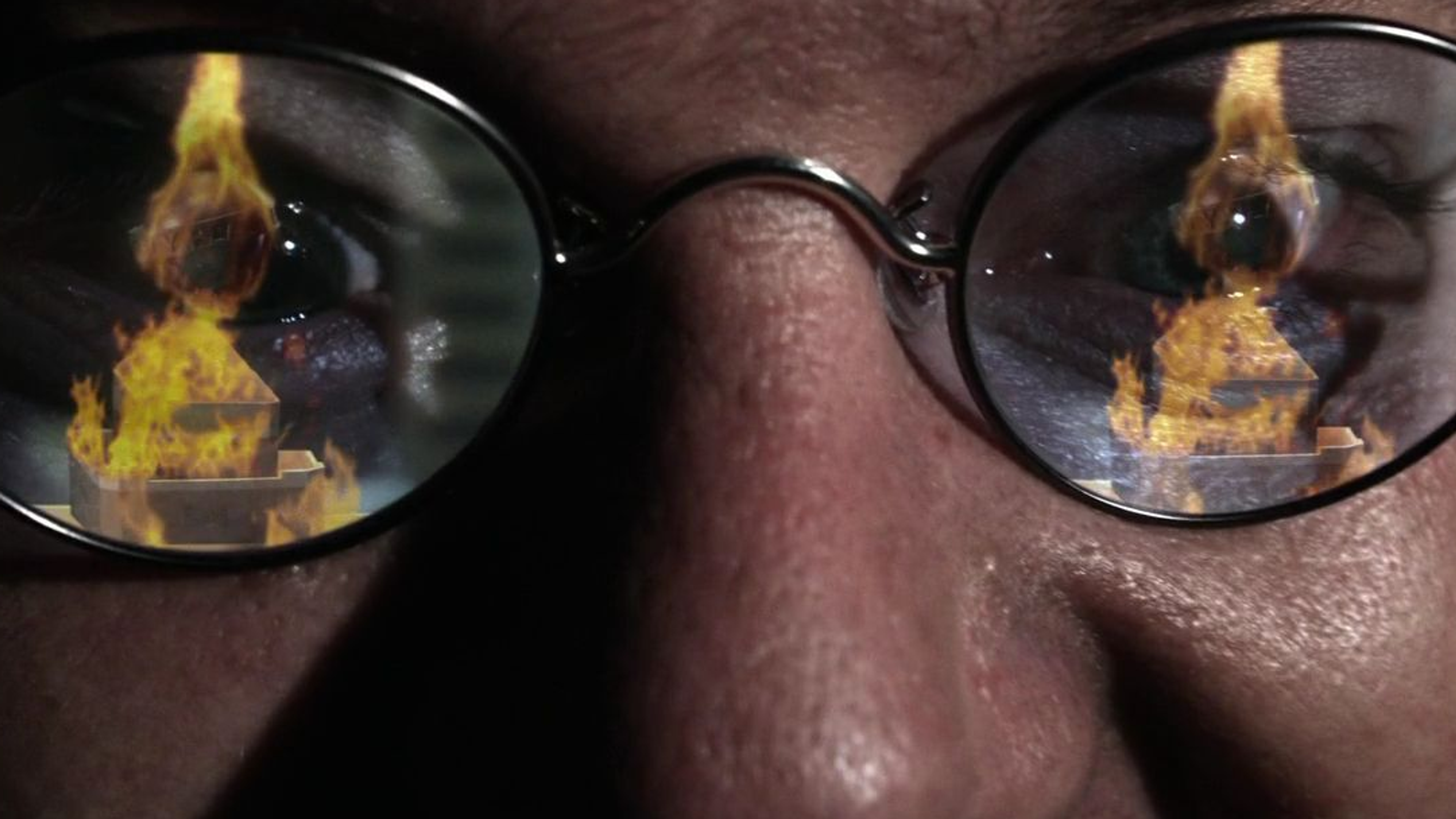 A model of the Daily Planet is on fire, reflected in a man's sunglasses.