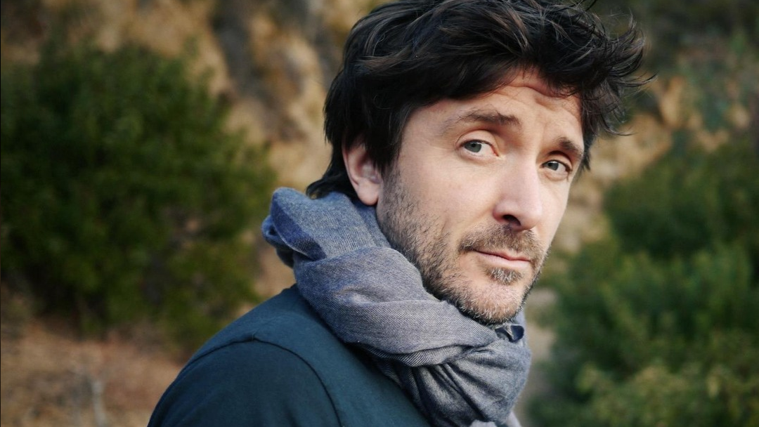 A man with dark hair is wearing a scarf.