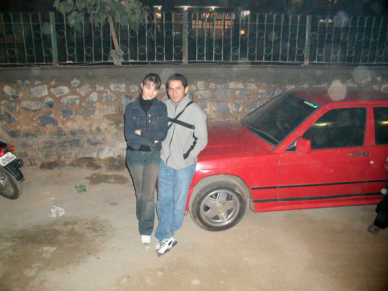 Dos viajeros junto a un automóvil rojo durante la noche.