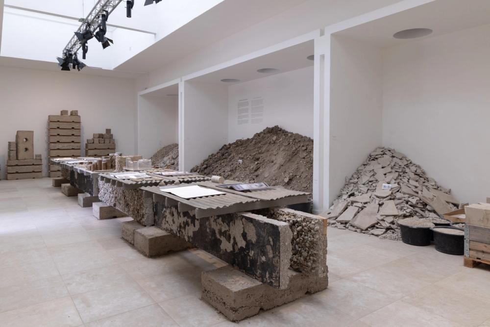 An image of piles of concrete, organized around the edges of a room with a makeshift concrete bench in the centre