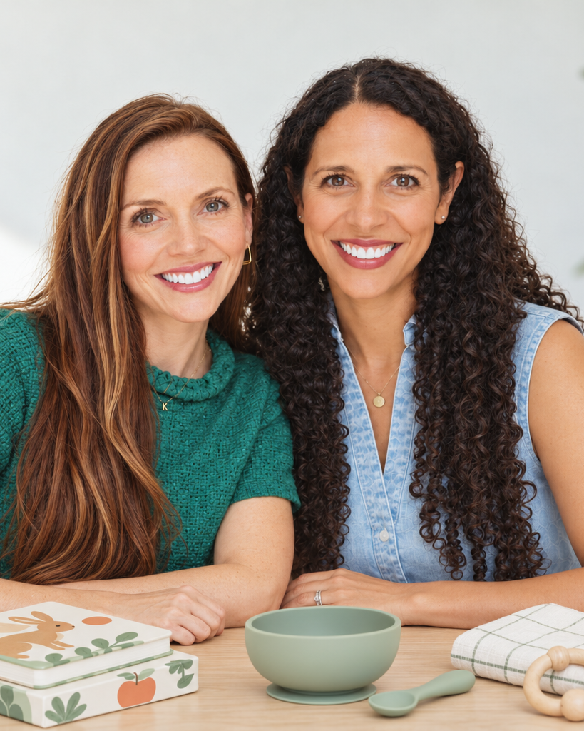 Ashley (left) and Chanel, the founders of Good & Growing Kids, smiling together at a kitchen table with a children's book and a sage silicone bowl.