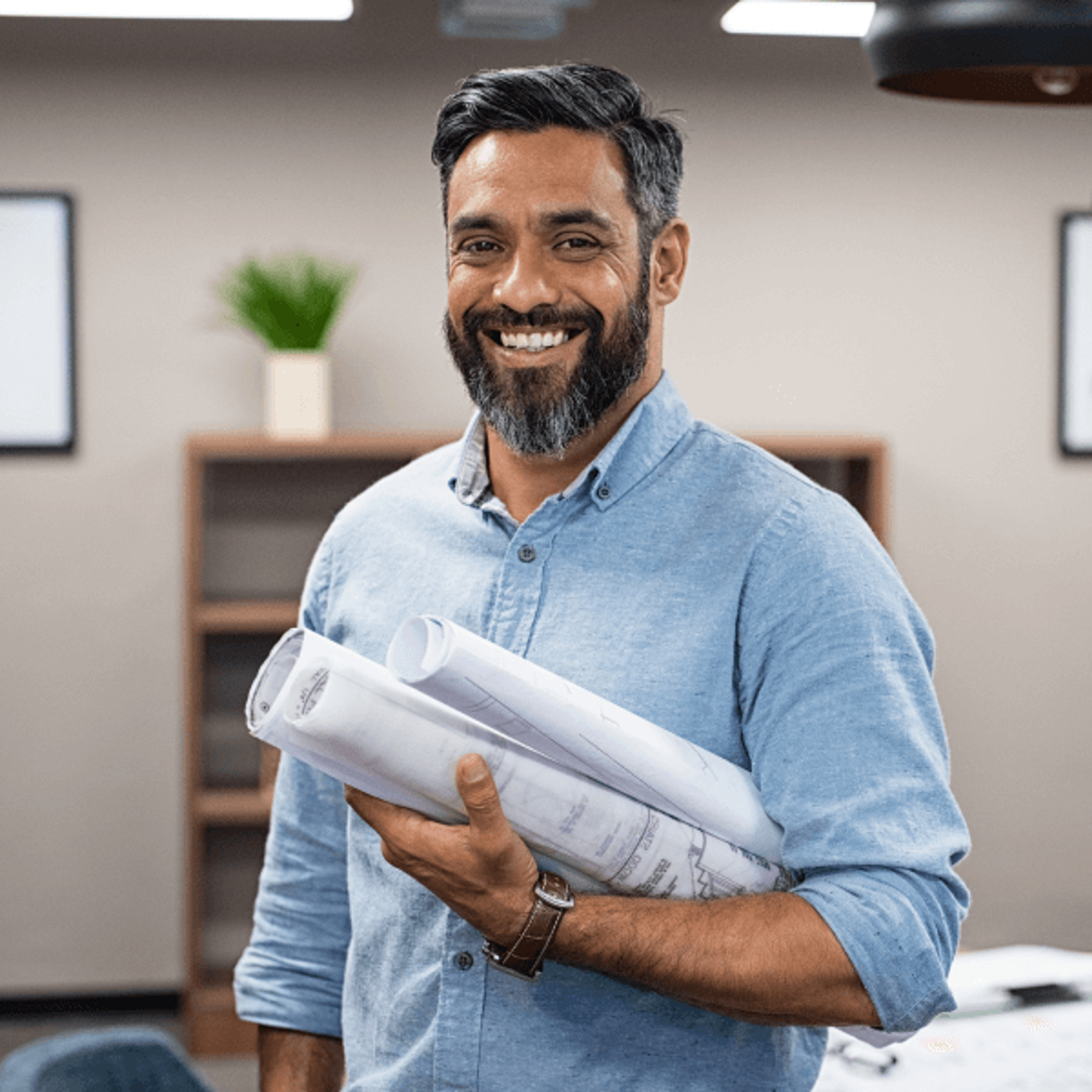 smiling man holding rolled blueprints in an office.