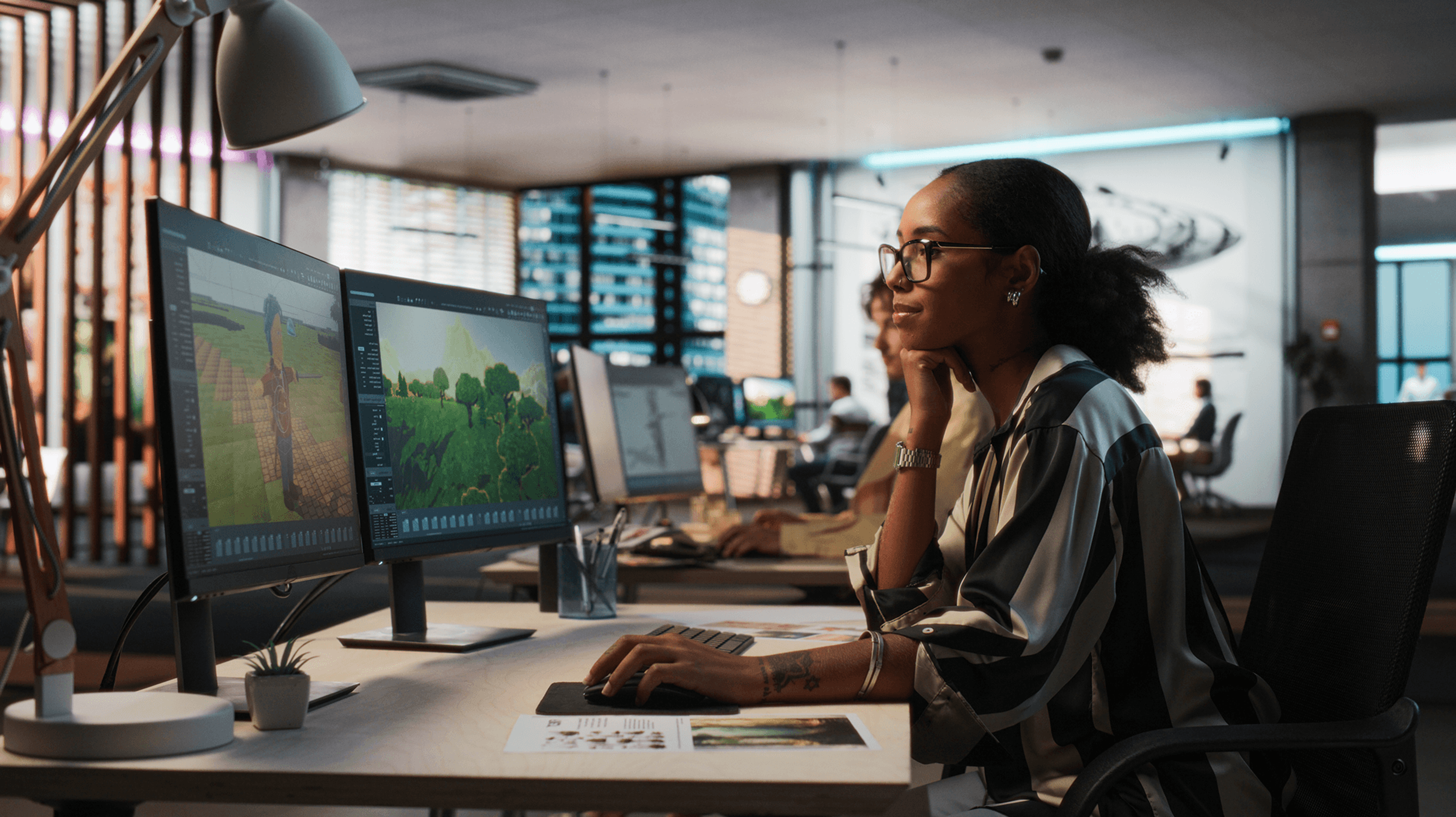 A woman works on dual monitors displaying 3D design software in an office.