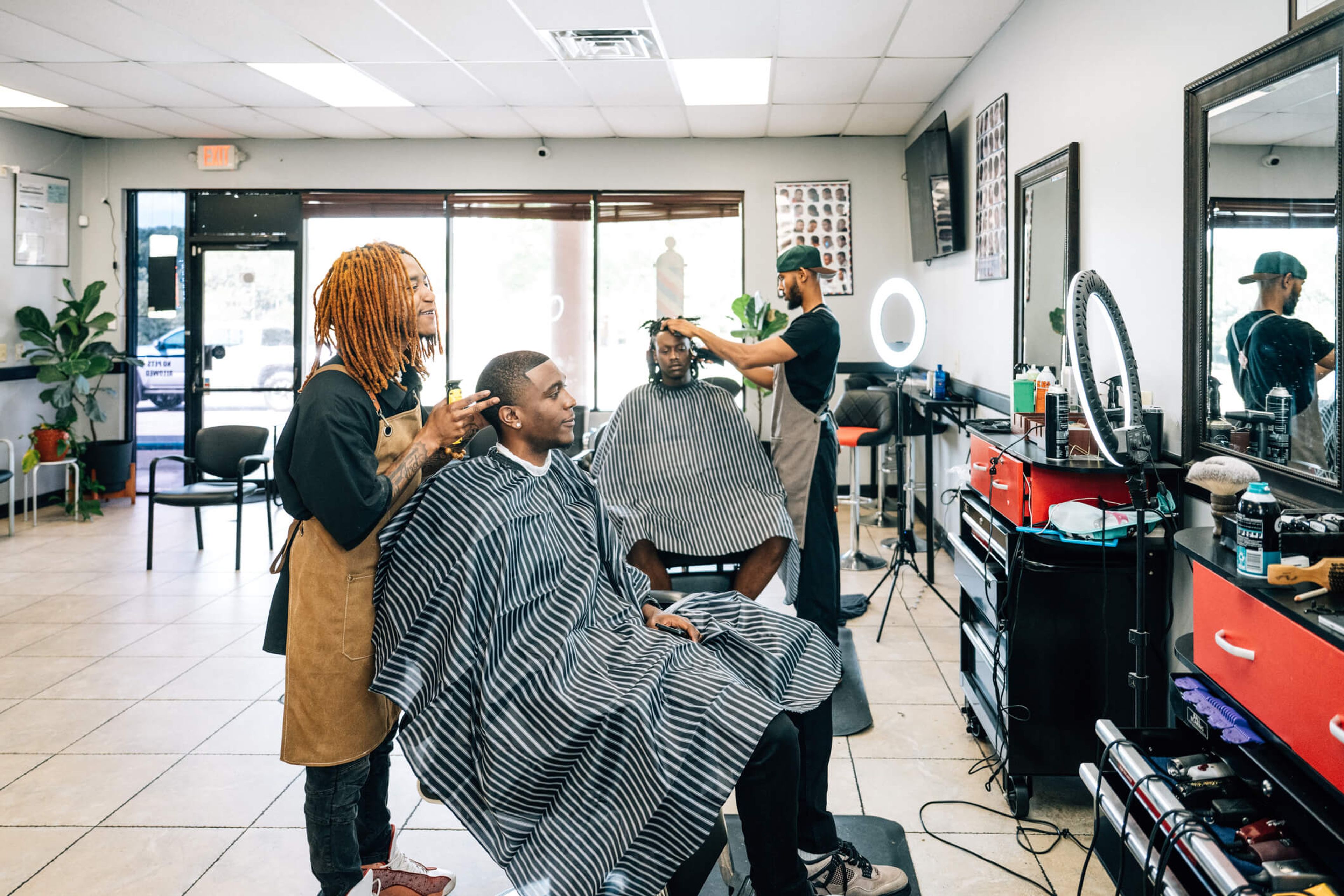 Two barbers cutting clients' hair in a barbershop.