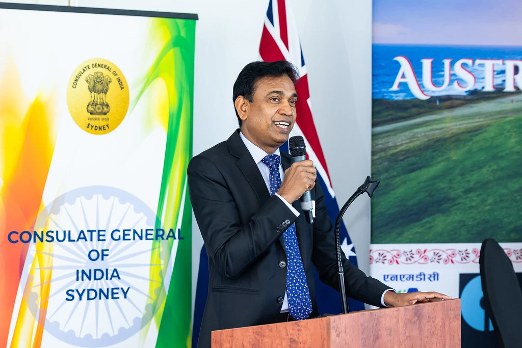 Dr. S. Janakiraman at a podium with a microphone, standing in front of India and Australia-themed banners.